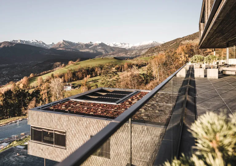 Outdoor balcony with a glass barricade, overlooking a large grassy valley and mountains