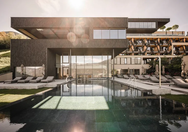 Outdoor pool surrounded by gray chairs, and a black and beige building with large windows in the back