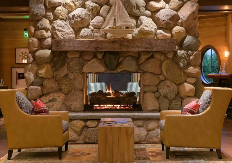 Indoor lodge-style room with a stone fireplace and two leather chairs in front