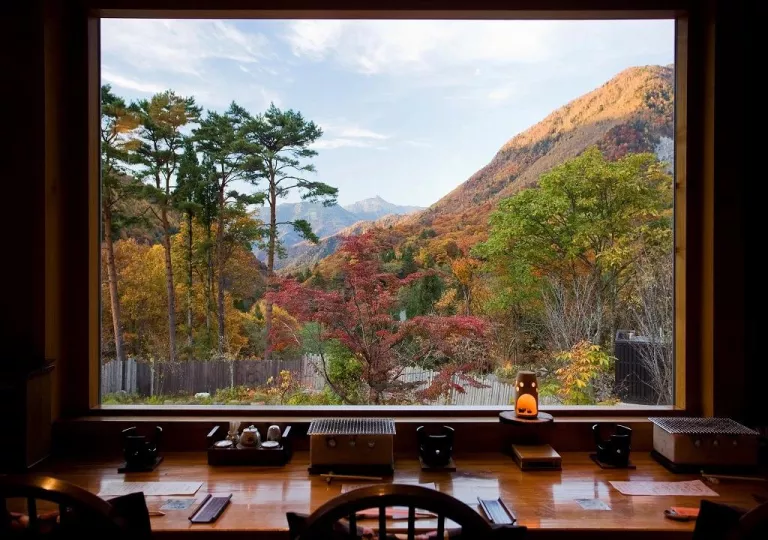 Desk in front of a large window, overlooking orange and green trees on a hill