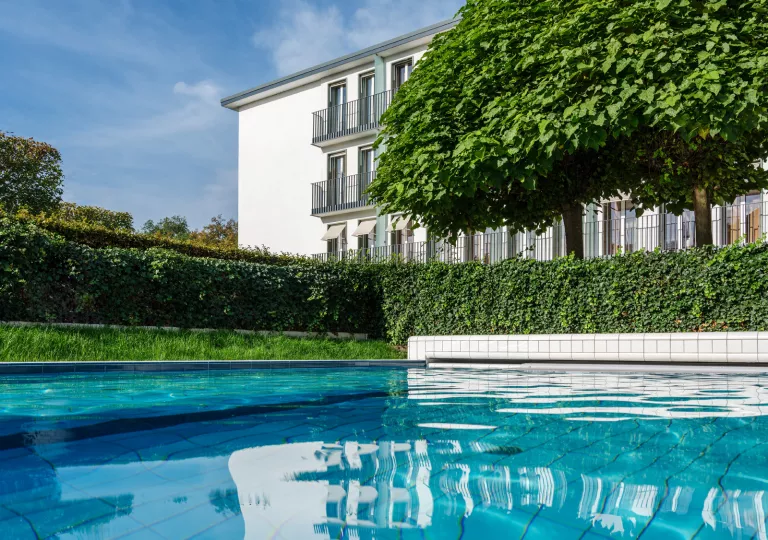 Outdoor pool with trimmed bushes and a white building in the background