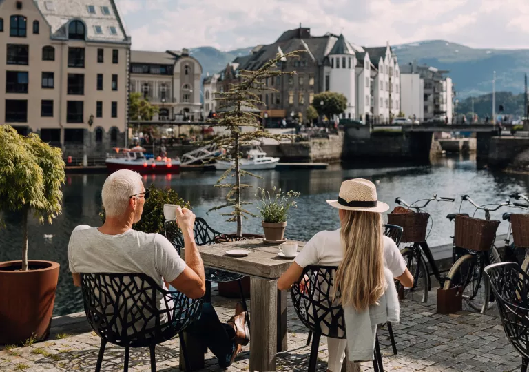Man and woman sitting on a stone patio, drinking coffee and looking out to a river