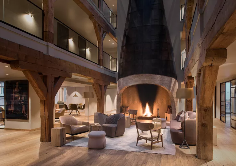 Indoor lobby and lounge with cushioned chairs in front of a large, stone fireplace