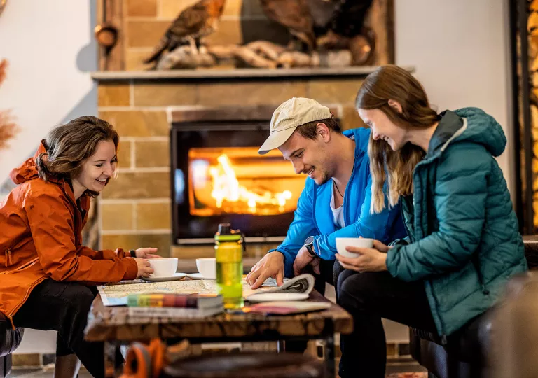 Man and two women sitting by a table in front of a fireplace, looking at a large map