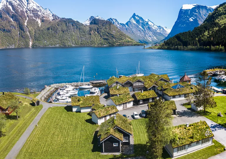 Sky view of small houses by a lake, with large mountains in the background