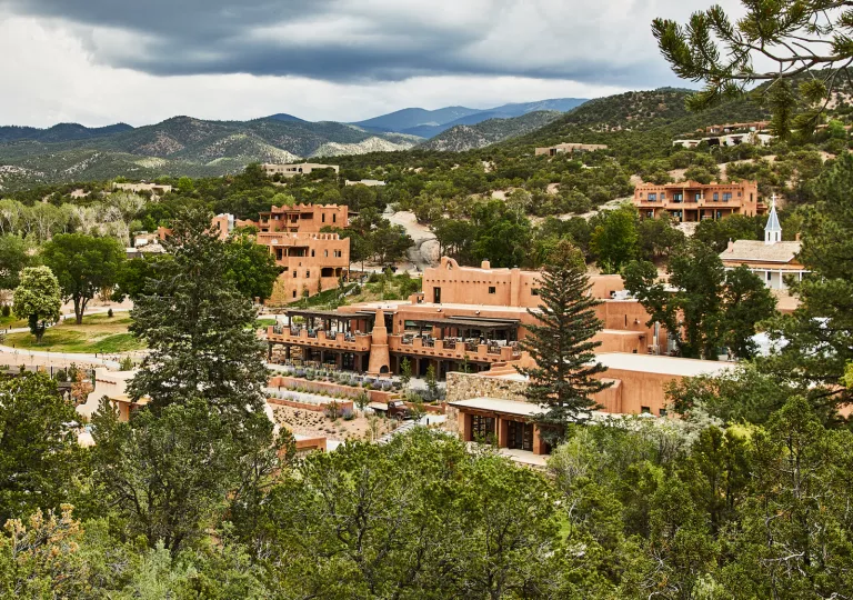 Exterior view  of orange building complex surrounded by tall trees and mountains