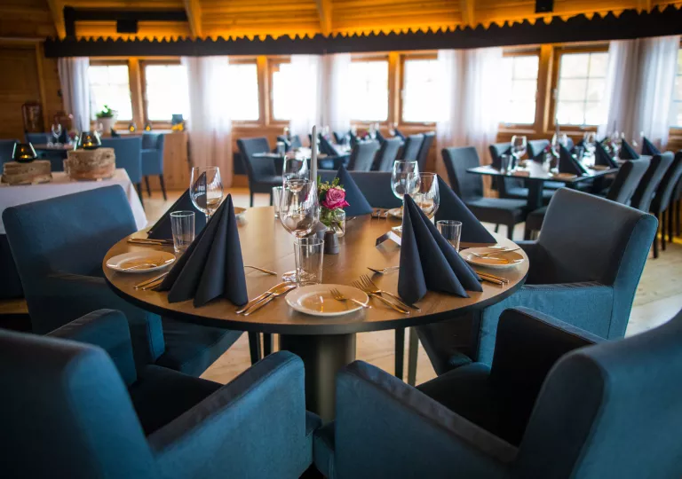 Dining hall with blue, cushioned chairs and table cloths, with wine glasses on each table
