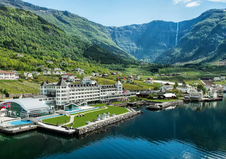Exterior, wide view of a white hotel complex in front of a port with boats in front