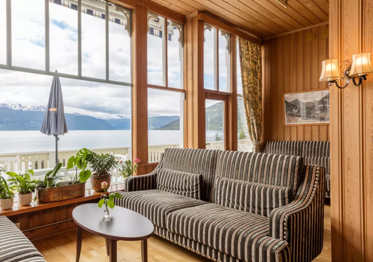 Corner room with wooden walls and striped couches, with a lake outside