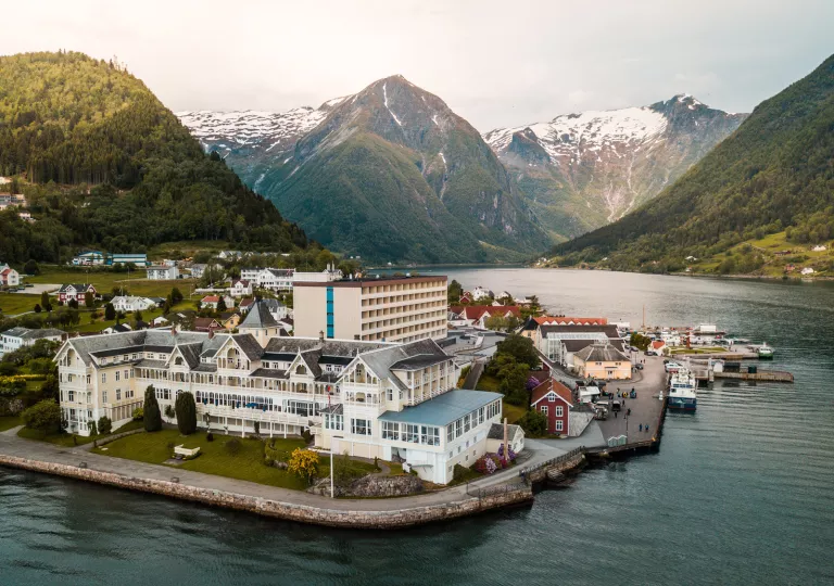 Exterior, sky view of a hotel complex with a lake in front and mountains in the background