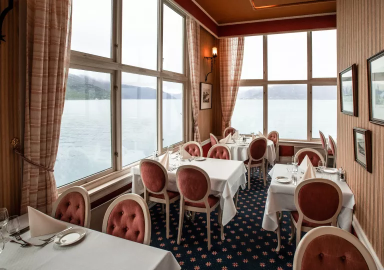 Restaurant in a corner room with large windows, red chairs and white tables