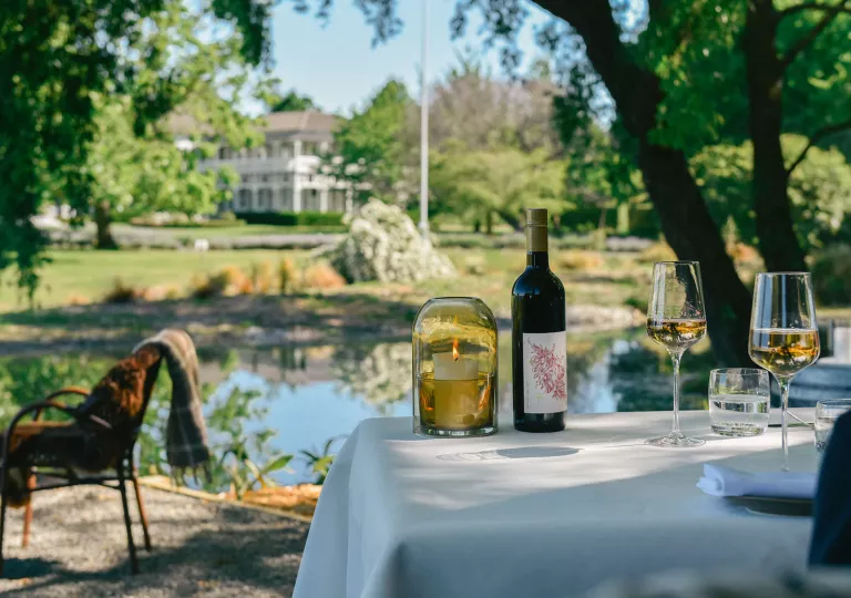 Bottle of wine and wine glasses on a white table looking out towards a lake