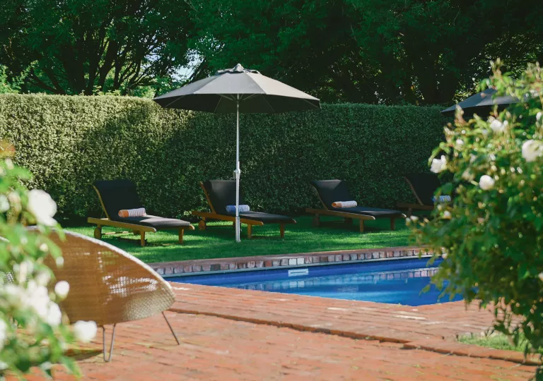 Outdoor pool surrounded by wooden chairs and trimmed hedges