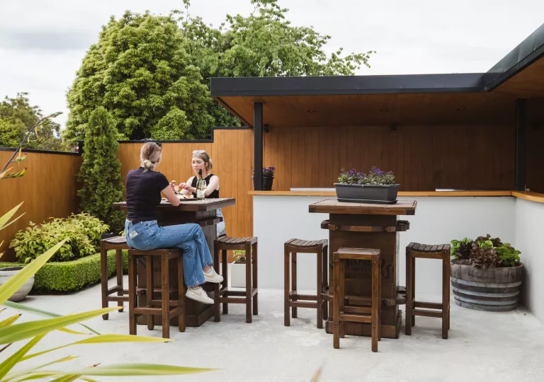 Outdoor patio with two people sitting on tall, wooden stools