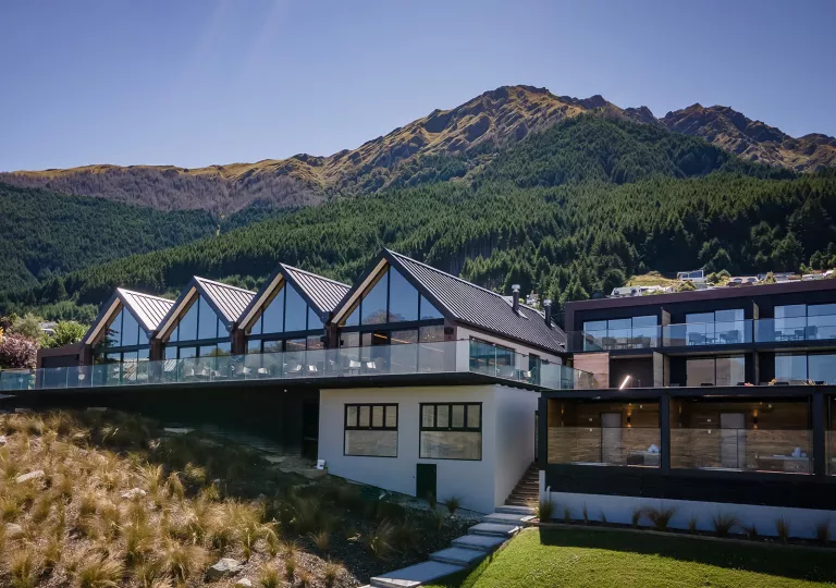 Exterior view of  a row of buildings with glass walls, and tall mountains in the background
