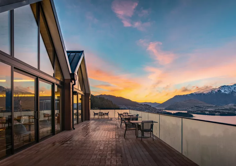 Outdoor balcony and patio, with a building with glass walls on the left and a lake to the right