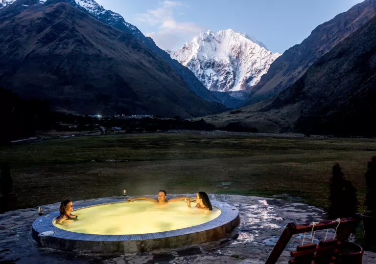 Outdoor hot tub with an illuminated yellow light, with snow capped mountains in the background