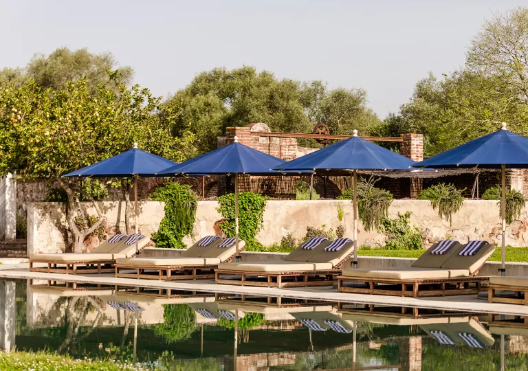 Outdoor pool surrounded by reclining chairs and blue umbrellas