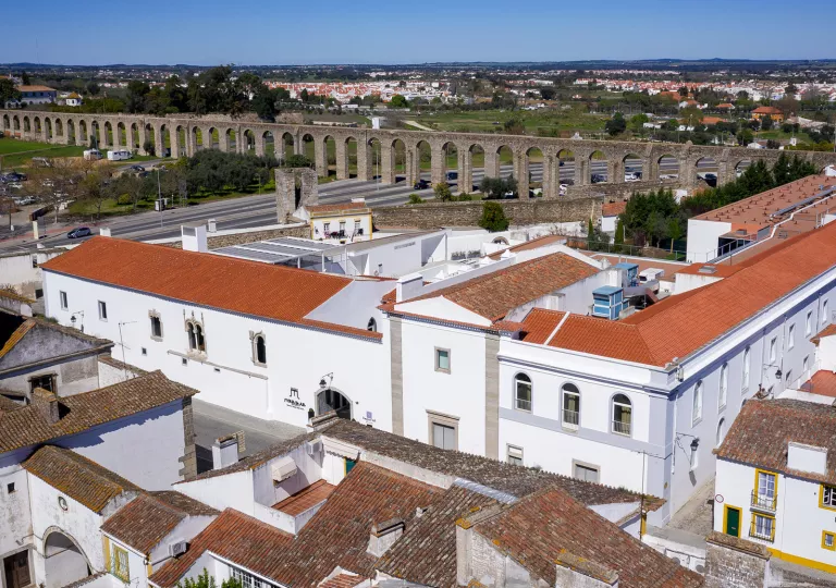 Exterior view of a large white building with red roofing, with a large stone bridge in the distance