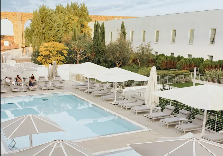 Outdoor pool surrounded by gray reclining chairs and white umbrellas