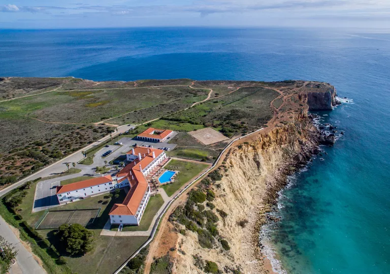 Sky view of white and red hotel building with a large cliff and ocean to the right