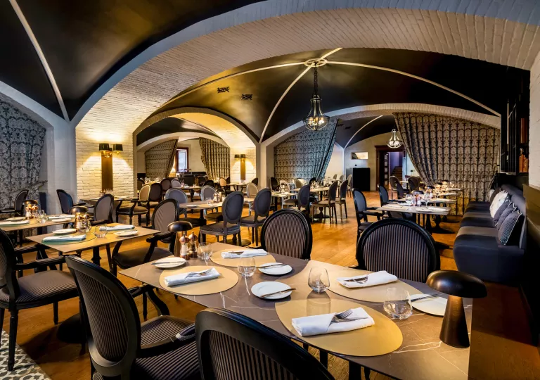 Restaurant dining hall with black cushioned chairs and large marble dining tables