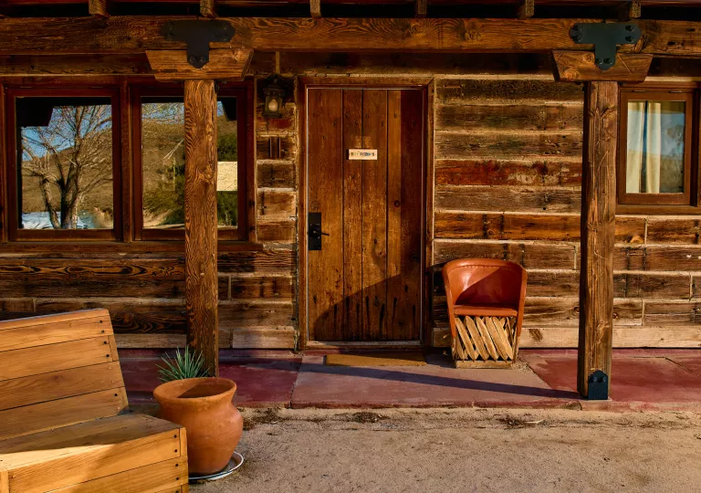 Exterior view of wooden lodge room with a leather chair and wooden bench in front