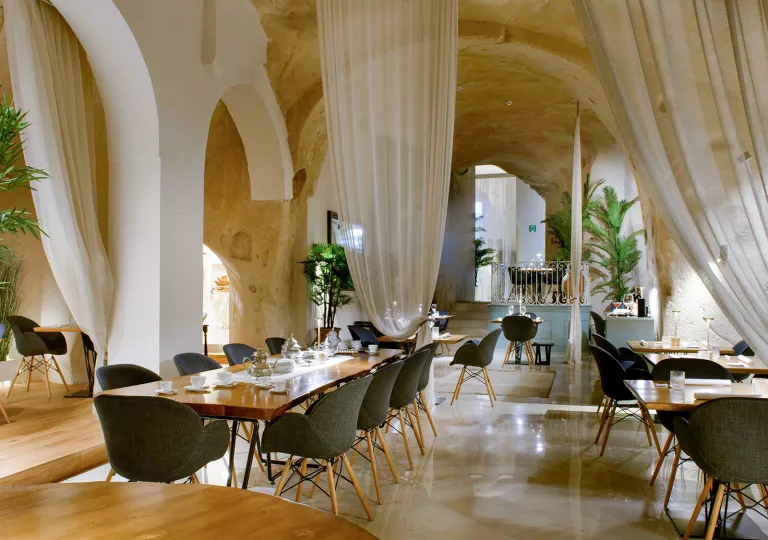 Indoor dining hall with long, rectangular tables and cushioned, gray chairs