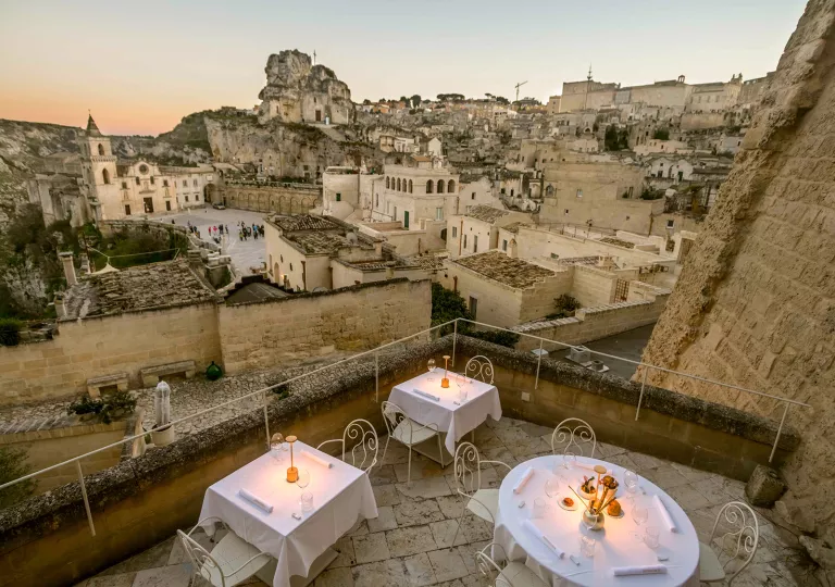 Outdoor balcony on a stone building with white dining tables, overlooking stone ruins and buildings