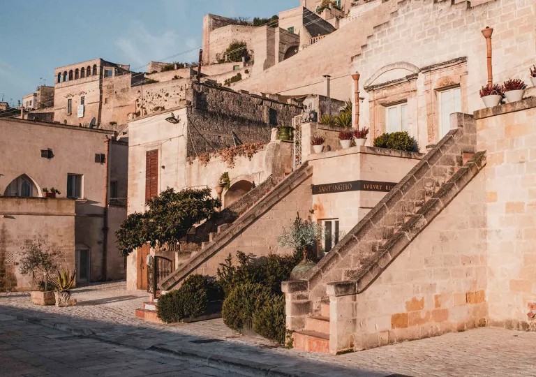 Exterior view of stone hotel building with 2 small staircases, bushes and small trees