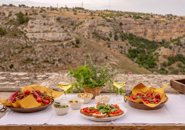 Table on the edge of a cliff with plates of toast and tomatoes, and two glasses of wine