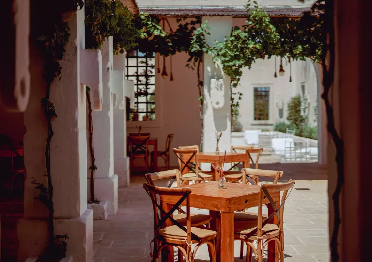 Outdoor patio with wooden tables and chairs, with large, white stone pillars