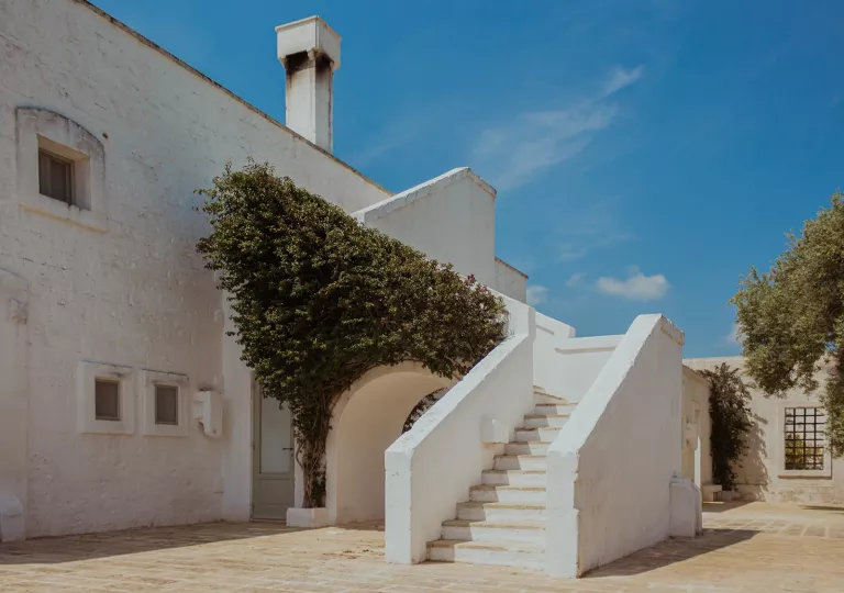 White, stone building with a staircase and bushy tree