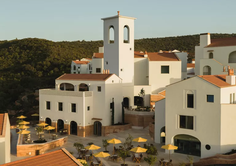 Exterior view of white hotel buildings with yellow umbrellas on the ground floor