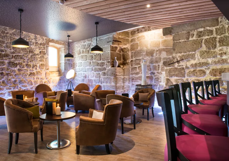 Tavern with cushioned chairs and circular tables, with stone walls