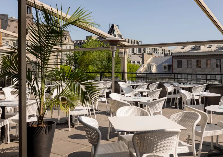 Outdoor patio with white tables and chairs, with town buildings in the background