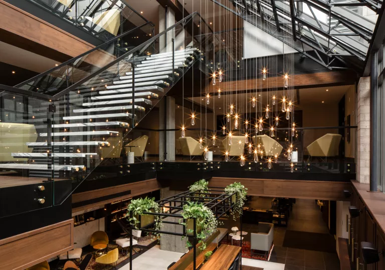 Hotel lobby with a staircase with glass walls and hanging lights