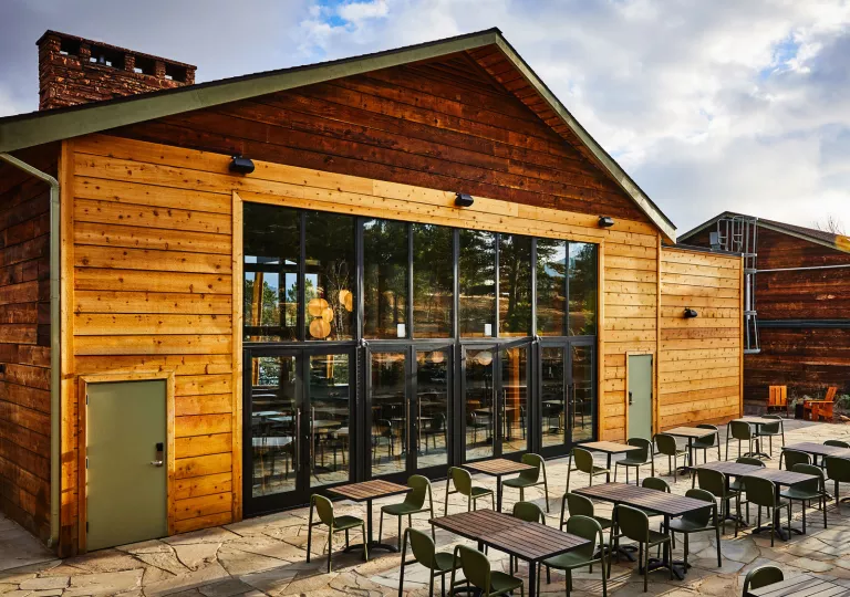Exterior view of wooden cabin building with large glass doors and dining tables outside