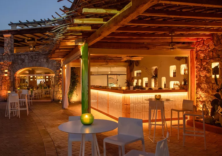 Outdoor bar and lounge with chairs and tables, and an illuminated bar