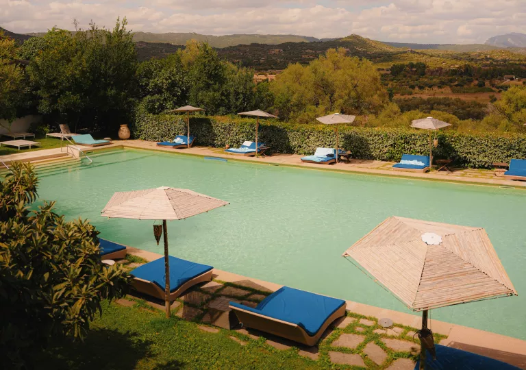 Outdoor pool with straw umbrellas and blue reclining beds surrounding the pool
