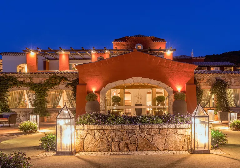 Exterior view of hotel building with stone archways and flowers in potted plants