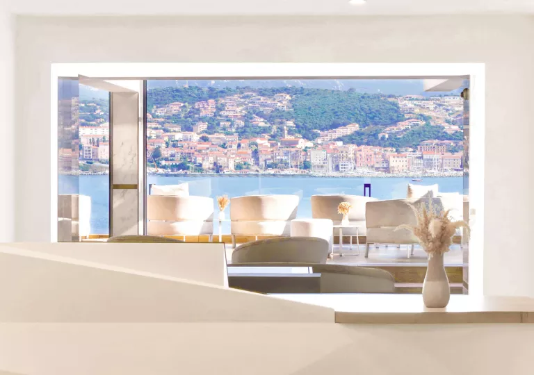 Cushioned white chairs on an outdoor patio looking out towards a large lake a distant town