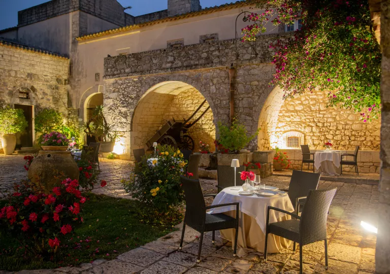 Outdoor patio and garden, with a stone building in the background and a dining table with black chairs