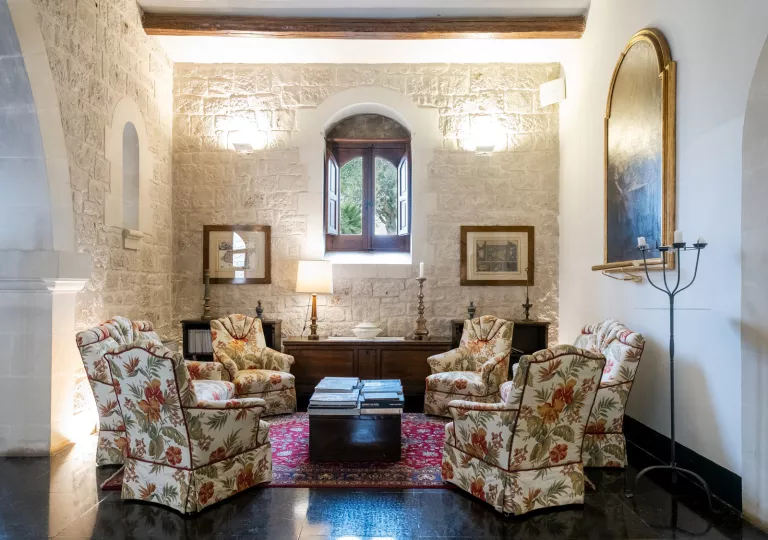 Seating area in a white, stone room, with cushioned chairs with flower patterns around a coffee table