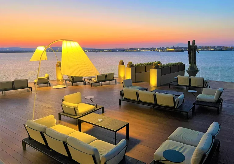 Outdoor patio with cushioned chairs, looking out towards the ocean and sunset