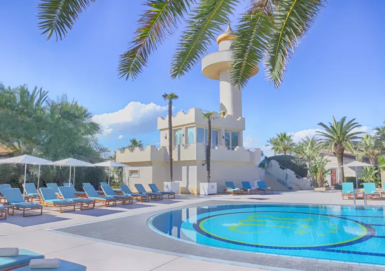 Exterior view of white building and an outdoor pool, surrounded by white chairs