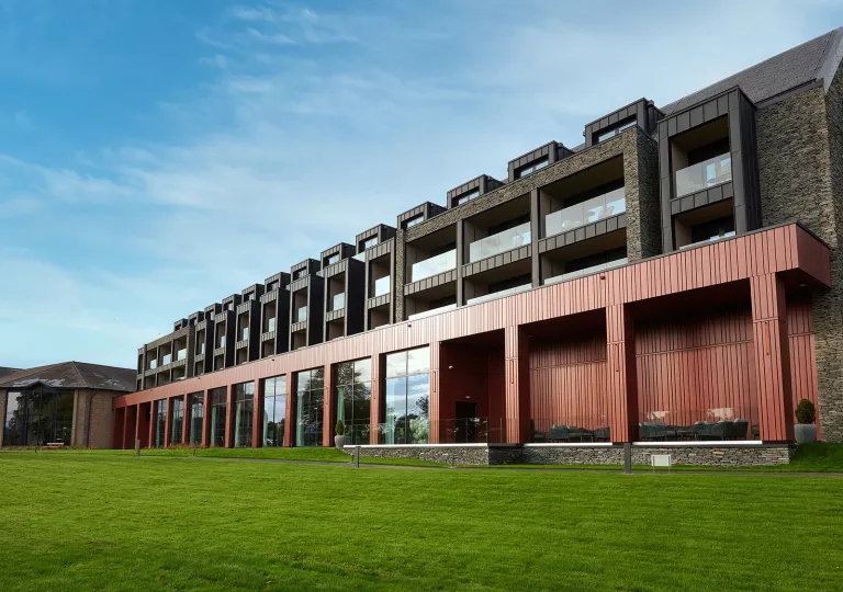Exterior view of a long red and black building, with a grass field in front