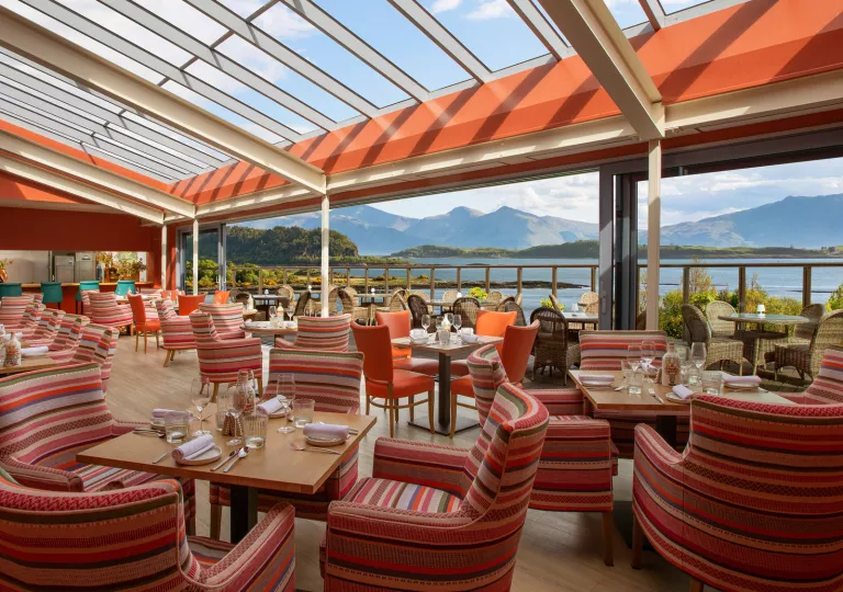 Outdoor dining area of a restaurant with striped red, cushioned chairs and square dining tables