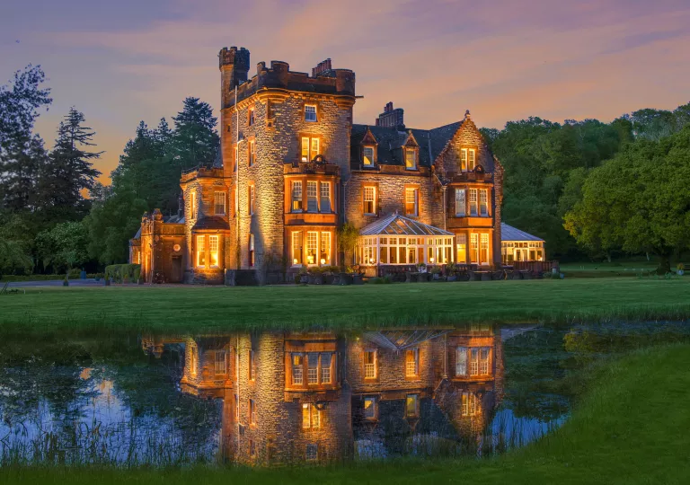 Illuminated, castle-like hotel building with a large grass field in front