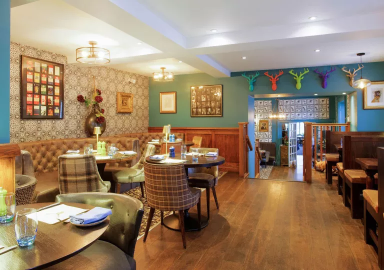 Dining area with multiple, circular tables and cushioned chairs, with a staircase to the right